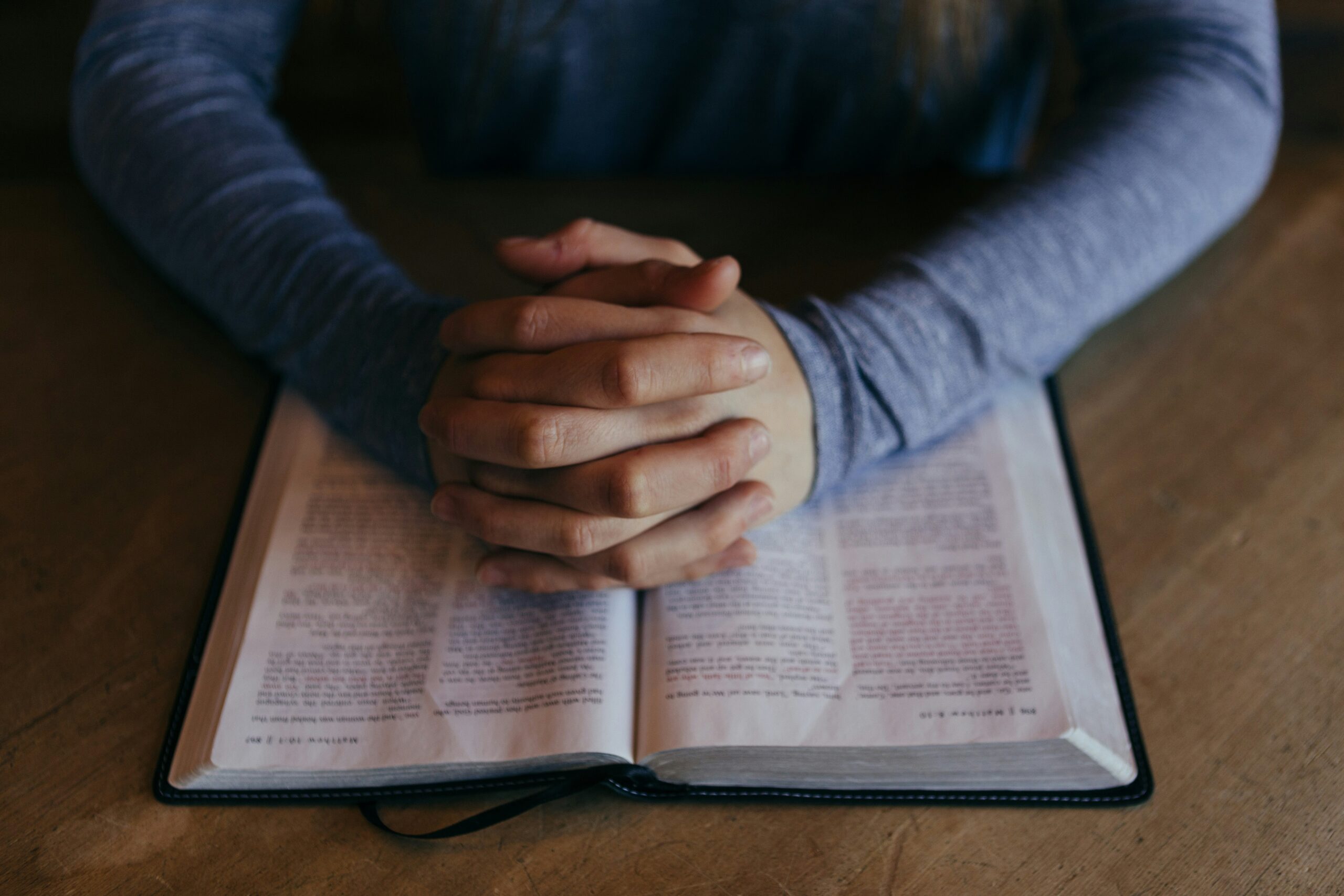 Person praying with clasped hands over an open Bible – World Prayer Center