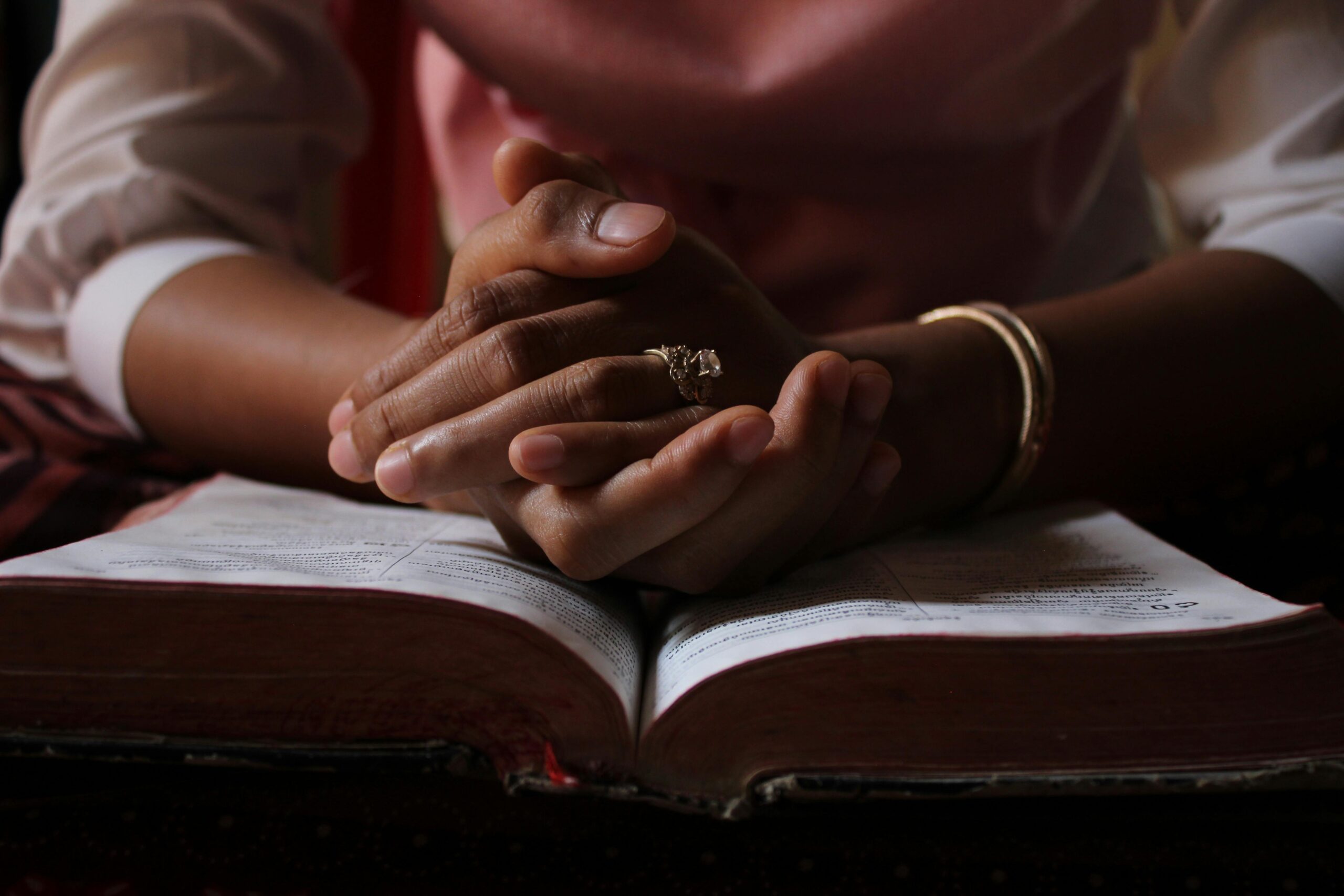 Hands folded in prayer over an open Bible during personal Christian devotion